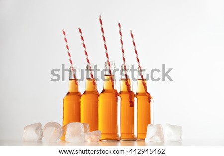 Opened bottles with cold lemonade inside and striped drink straws isolated on white in center between ice cubes