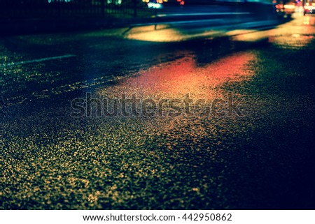 Vintage style - Rainy night in the big city, the light from the headlamps of vehicles approaching on the road. Close up view from the level of asphalt, focus on the asphalt