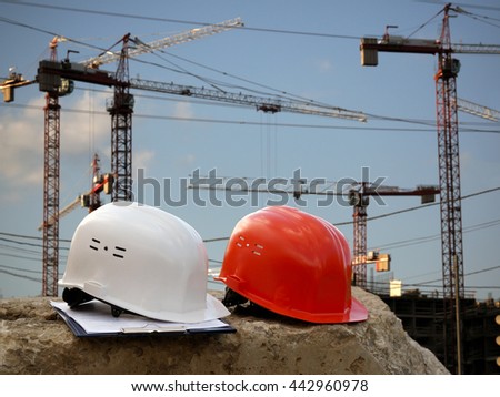 Building helmet on a background of cranes, construction. Helmets orange working and white - helmet engineer. The tablet with papers. Blue sky, plenty of sun