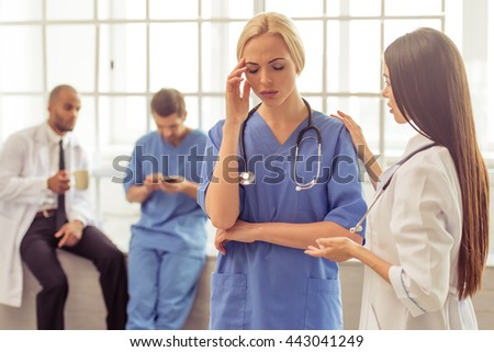 Beautiful female doctor is keeping hands on temple, having headache. Asian doctor is calming her. Male doctors in the background