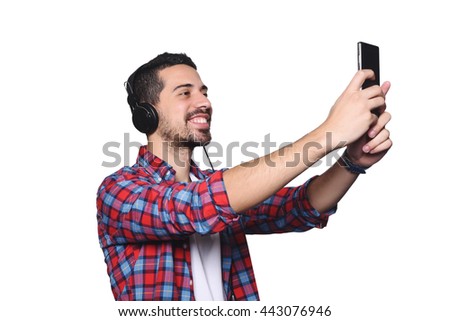 Portrait of attractive young man taking a selfie with his smartphone and black headphones. Isolated white background.