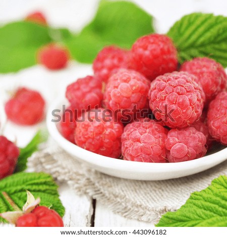 Sweet fresh ripe sweet raspberries in plate with daisies on wooden background, selective focus