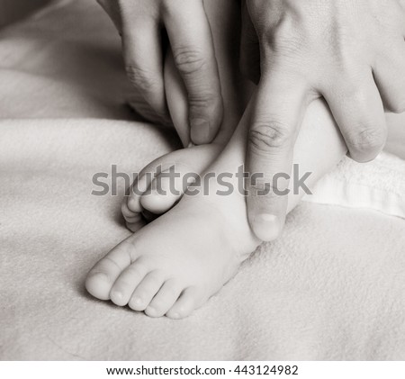 black and white picture of the hands of a woman doing her baby foot massage at home