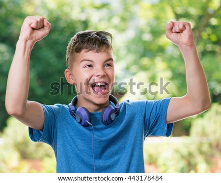 Victory screaming teen boy 12-14 year old. Winner boy with headphones and sunglasses posing outdoors.