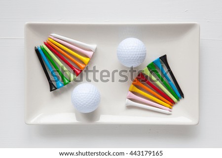 White ceramic dishes with golf balls and wooden tees on over white background, rectangle dish