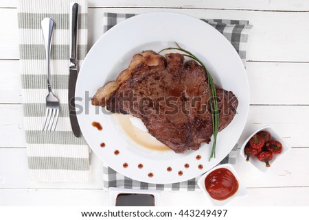 fresh rich juicy grilled beef meat steak fillet on white plate over wooden table decorated with sauces and cutlery new york style