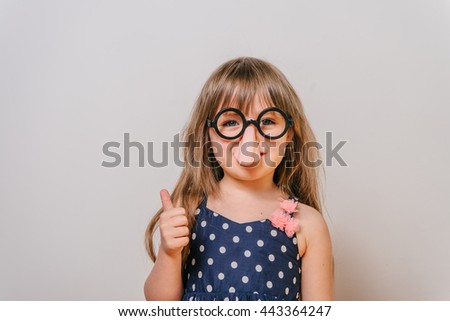 a little girl with glasses. funny glasses humor. little girl laughing. girl clown. Girl looks funny. Girl showing thumbs up. all perfectly.