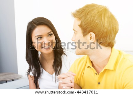 Young happy couple holding hands and looking each other on the couch in living room