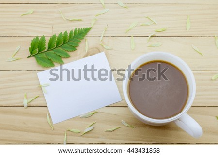Coffee mug with green foot fern and notes on yellow rustic table. 