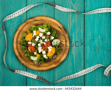 Diet plan - salad of fresh vegetables and tape measure on a white wooden table