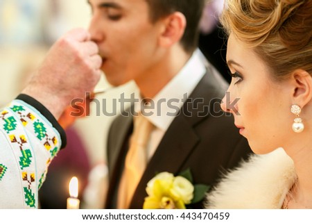 Bride looks at a groom while he kisses a wedding ring helb by a priest