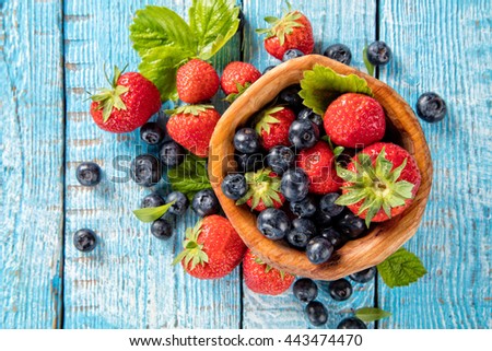 Fresh berry fruit pile in bowl with leaves placed on old wooden planks. Shot from aerial view