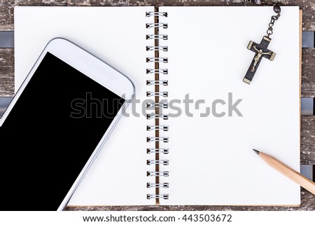 smart phone or cellphone with recycle notebook paper and cross necklace over grunge wooden table background.
