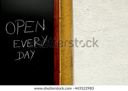 Sign "Open every day" written with white chalk on blackboard on the city building wall