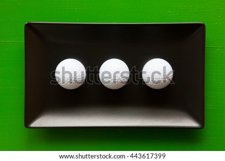Black ceramic dishes with golf balls on over green background, rectangle dish