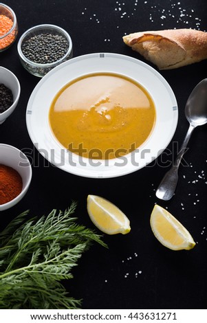 Cream soup of assorted lentil. Yellow and green lens, spices as raw for meal and lemon on black background. Healthy, appetizing, delicious, vegetarian food. Top view, copy space.
