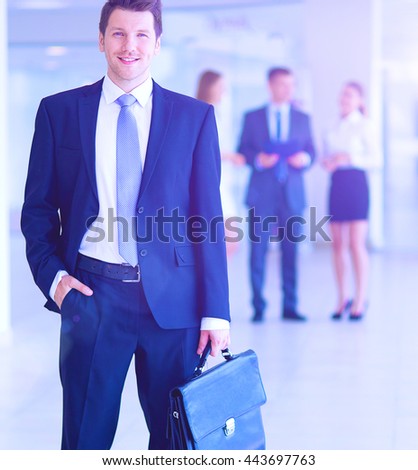 Portrait of young businessman in office with colleagues in the background and using mobile