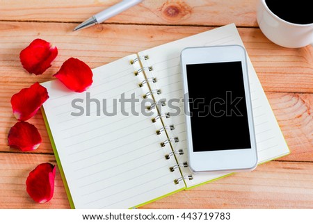 Smart phone on blank notebook with Rose petals on wood background abstract texture background for your design