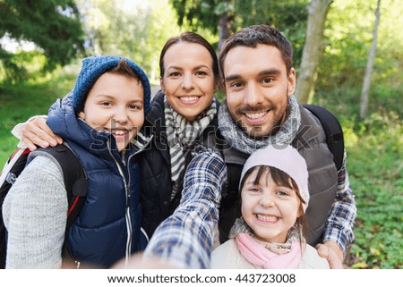 technology, travel, tourism, hike and people concept - happy family with backpacks taking selfie and hiking