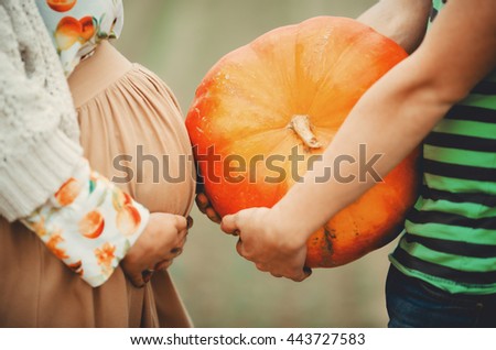 Man holds a pumpkin standing behind a pregnant woman Royalty-Free Stock Photo #443727583