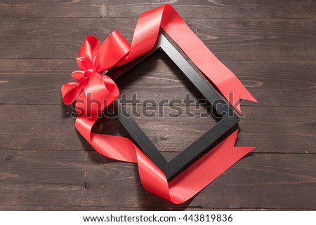 Frame picture and ribbon are on the wooden background with empty space.