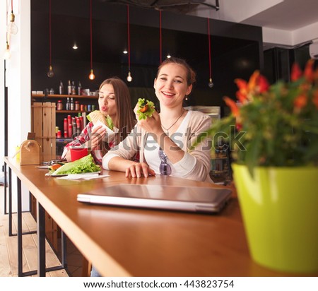 Toned picture of pretty ladies sitting in cafe. Happy girls eating sandwiches or snacks during break.