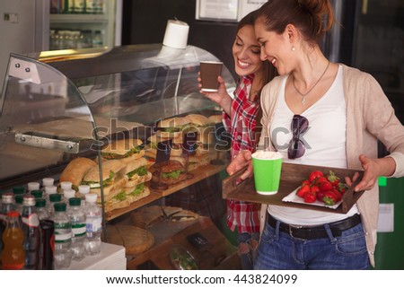 Toned picture of beautiful ladies choosing delicious and tasty dishes in cafe or restaurant. Happy ladies smiling and communicating what to buy.