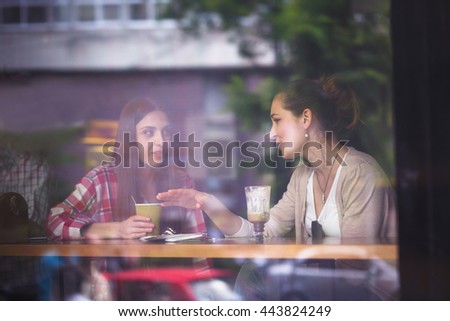 Toned image of pretty girls communicating and talking while eating hamburgers or sandwiches, drinking coffees in cafe or restaurant.