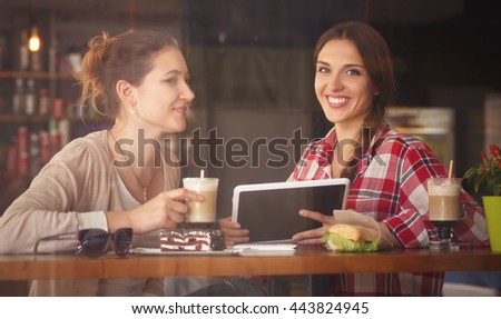 Toned image of best friends communicating or talking while sitting in restaurant or cafe. Ladies looking at tablet PC.