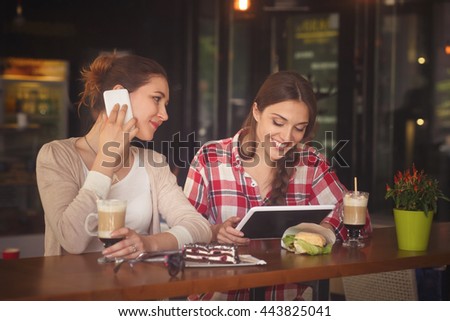 Toned picture of beautiful lady in love communicating over mobile or smart phone while her best friend girl using table PC in cafe or restaurant.