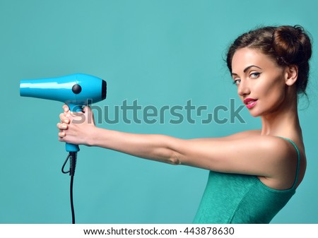 Happy young curly brunette woman with hair dryer on blue mint background. Hair style beauty concept Royalty-Free Stock Photo #443878630