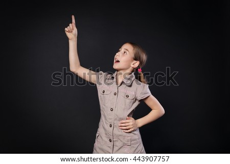 Small girl has an idea. Child shows finger up as an eureka, inspiration sign. Smart schoolgirl studio portrait at black background, school study and getting knowledge concept.