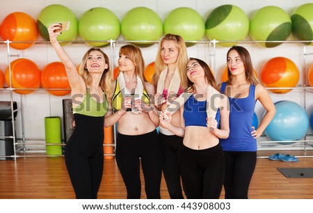 Making selfie. Group of girls in fitness class at the break looking at cell phone, happy and smiling. Woman friendship, healthy modern life of young people concept.