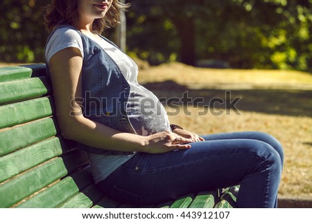 Pregnant woman sitting on a bench. on background nature. warm weather. Pregnant woman feeling the baby, warm sunny picture