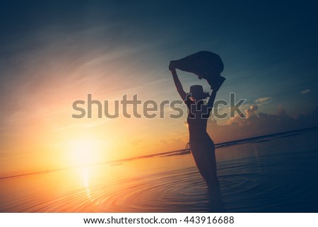 Silhouette of woman with shawl watching the sun rising over the horizon at the ocean