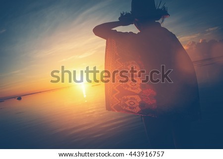 Woman's silhouette in hat looking the sun rising over the horizon (lens flare effect and vintage color)