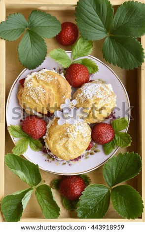 Homemade cream puffs or profiterole filled with whipped cream, powdered sugar topping served with strawberries in a wooden tray