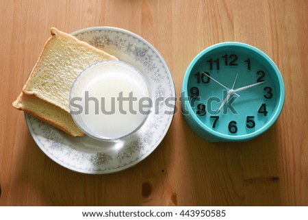 fresh milk in glass and bread in plate with green clock on wood table for refresh in morning