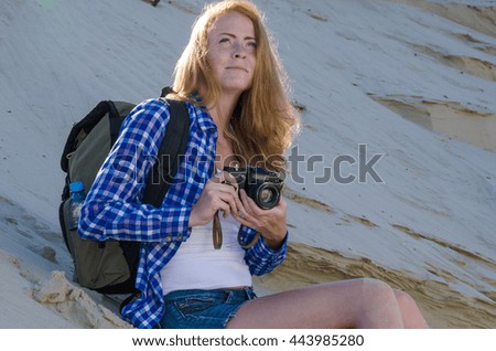 Young beautiful woman backpacker with red hair and freckles traveling in the desert and making pictures with vintage film camera. Sandy dunes background. Travel, adventure, freedom concept. Toned.