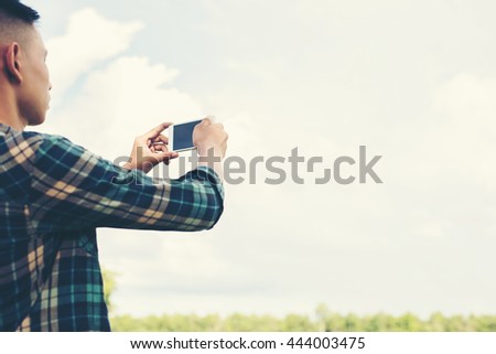 Young hipster man using smartphone taking the landscape photography in the grassland.
