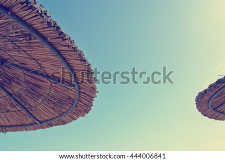 Low angle view on two straw parasols on the beach, on a sunny day, with blue sky in the middle. Can be used as summer background. Image filtered in faded, retro, Instagram style with soft focus.