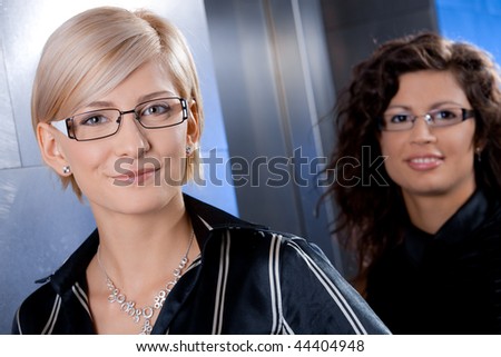 Closeup portrait of attractive young businesswomen, standing in office lobby, smiling.