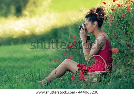 Young woman photographing with a poppy field in a red dress
