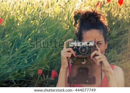 Young woman photographing with a poppy field in a red dress at sunset