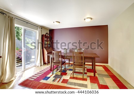 Cozy dining room with brown wall and colorful rug. Furnished with wooden table set and antique cabinet. Door exit to the backyard.