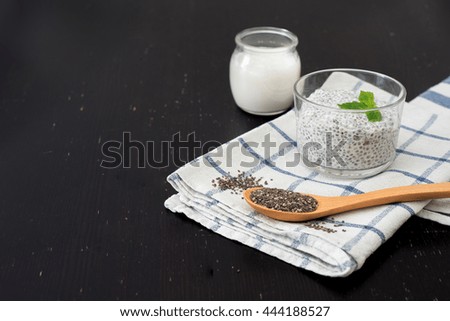 Chia pudding with blueberries on striped canvas, chia seed spoon and almond milk glass, dark wood background