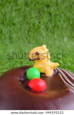 Dinosaur with eggs, made from sugar. On chocolate nest. All is edible. Isolated on artificial green grass background. Dinosaur and pre-historical concept. Art of cooking