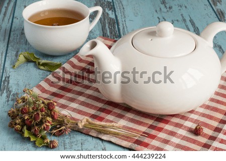  Teapot on a napkin, a cup and sprigs of the dried of wild strawberry on a blue wooden background.