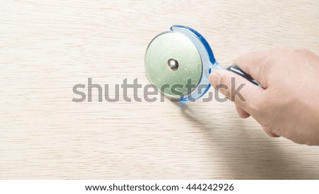Hand holding transparent blue color plastic pizza cutter or knife slicer on wooden table. Slightly de-focused and close-up shot. Copy space.