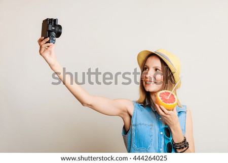 Summer vacation and happy people concept - girl taking self picture selfie with camera while holding citrus fruit in hand